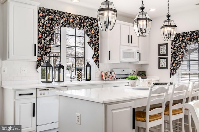 kitchen with white appliances, white cabinetry, hanging light fixtures, sink, and backsplash