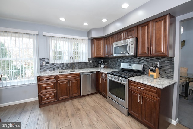 kitchen with sink, light hardwood / wood-style flooring, stainless steel appliances, light stone counters, and decorative backsplash