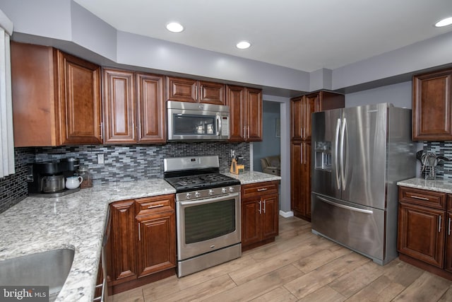 kitchen featuring tasteful backsplash, stainless steel appliances, light stone countertops, and light wood-type flooring