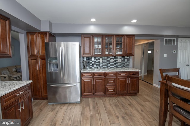 kitchen featuring tasteful backsplash, stainless steel fridge, light stone countertops, and light hardwood / wood-style floors