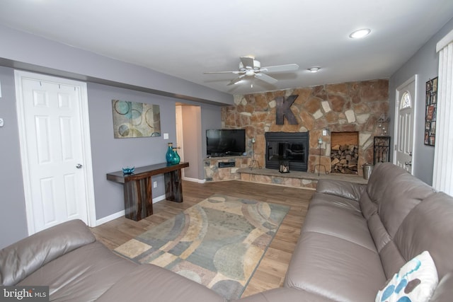 living room with a stone fireplace, light hardwood / wood-style flooring, and ceiling fan