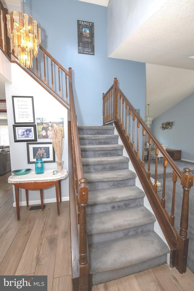 staircase featuring lofted ceiling, hardwood / wood-style floors, and a notable chandelier