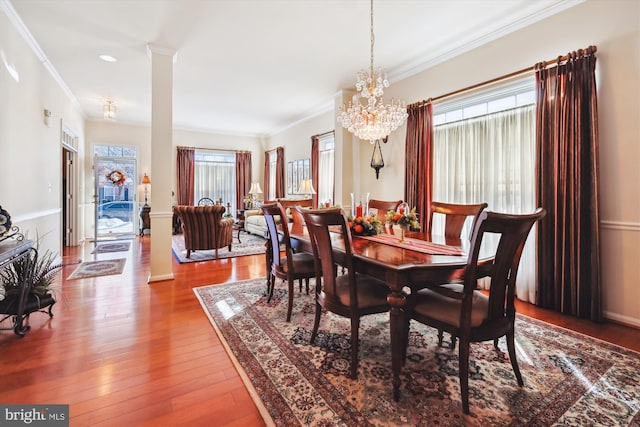 dining space with hardwood / wood-style flooring, decorative columns, ornamental molding, and a notable chandelier