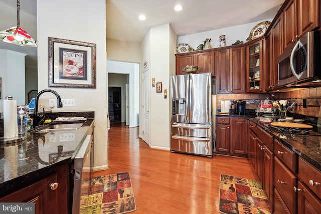 kitchen featuring appliances with stainless steel finishes, decorative light fixtures, tasteful backsplash, sink, and light hardwood / wood-style flooring