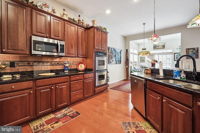 kitchen with light hardwood / wood-style floors, sink, decorative light fixtures, backsplash, and stainless steel appliances