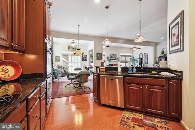 kitchen with dishwasher, light wood-type flooring, dark stone countertops, sink, and decorative light fixtures