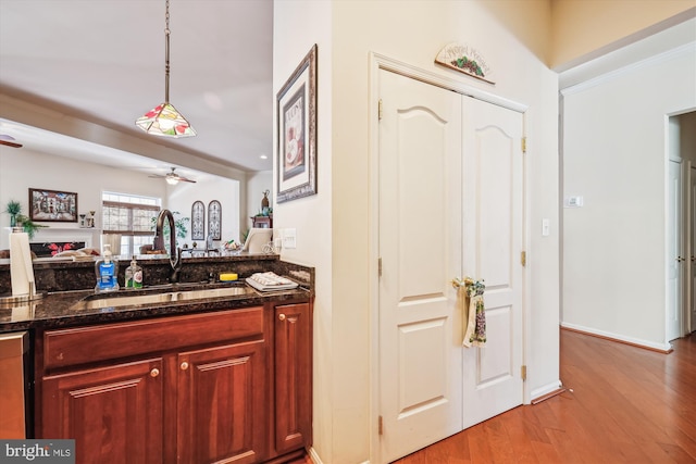 kitchen featuring pendant lighting, dark stone counters, sink, light wood-type flooring, and ceiling fan