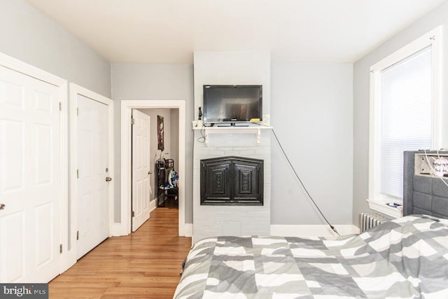 bedroom featuring radiator, light hardwood / wood-style flooring, and multiple closets