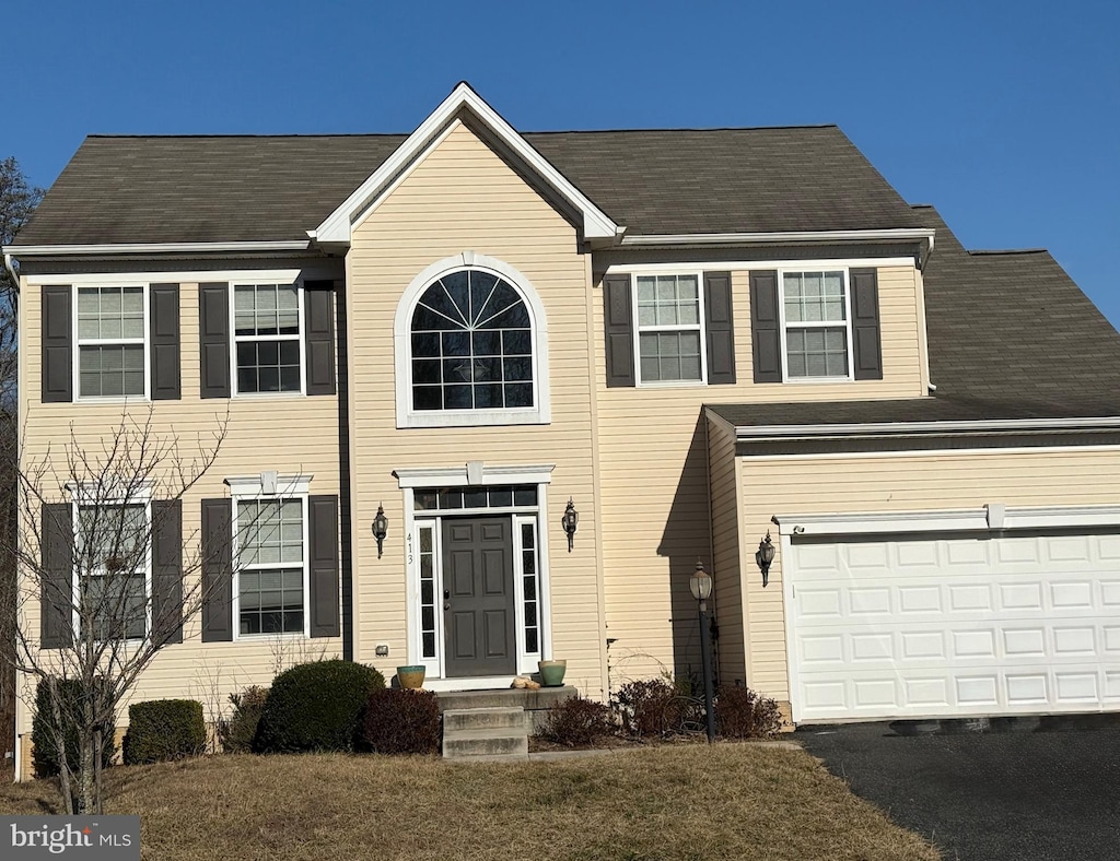 colonial house featuring a garage, aphalt driveway, and a front lawn