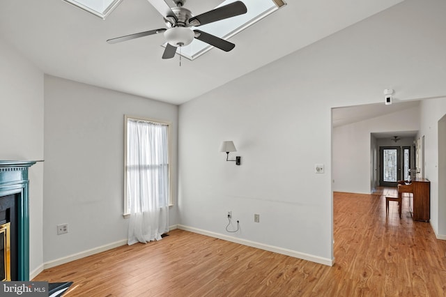 unfurnished living room featuring ceiling fan, lofted ceiling with skylight, and light wood-type flooring