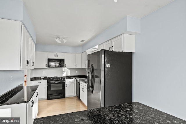 kitchen with white cabinets, dark stone counters, light hardwood / wood-style floors, and black appliances