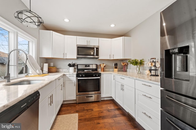 kitchen featuring dark wood-type flooring, sink, white cabinetry, decorative light fixtures, and appliances with stainless steel finishes