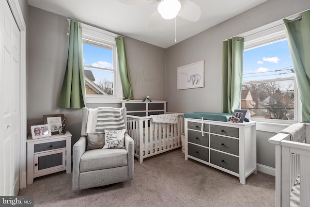 carpeted bedroom featuring a nursery area and ceiling fan