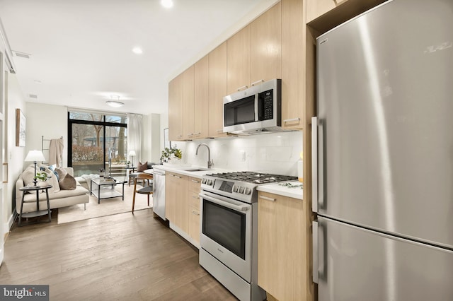 kitchen with wood-type flooring, sink, decorative backsplash, stainless steel appliances, and light brown cabinets