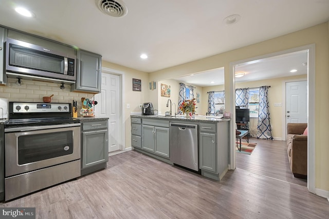 kitchen with appliances with stainless steel finishes, gray cabinetry, light hardwood / wood-style flooring, and backsplash