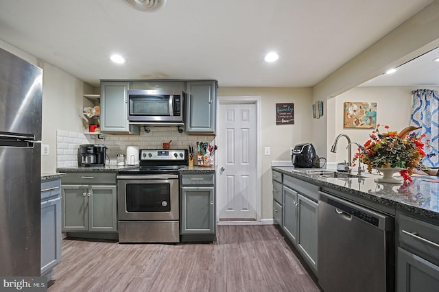 kitchen featuring appliances with stainless steel finishes, wood-type flooring, dark stone counters, decorative backsplash, and sink