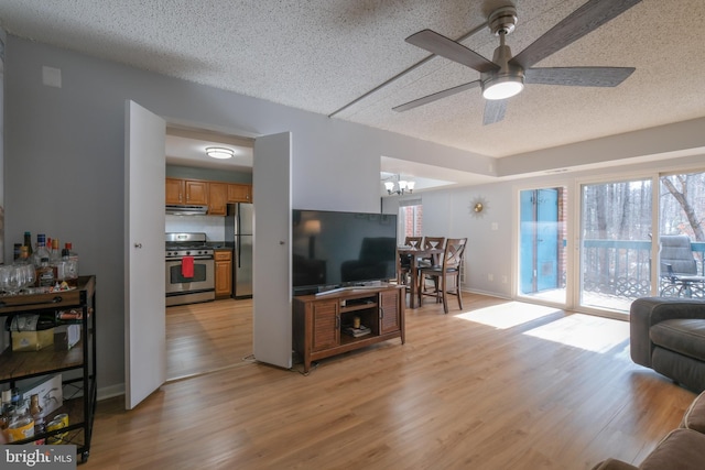 living room with ceiling fan with notable chandelier, light hardwood / wood-style floors, and a textured ceiling