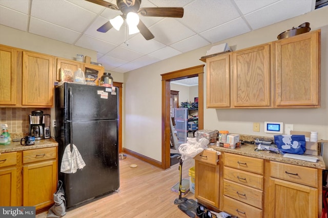 kitchen featuring tasteful backsplash, ceiling fan, a drop ceiling, light hardwood / wood-style floors, and black fridge