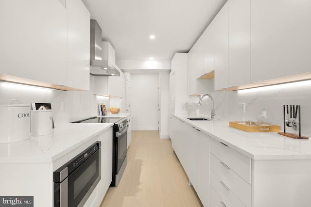 kitchen featuring stainless steel electric stove, built in microwave, wall chimney range hood, white cabinets, and sink