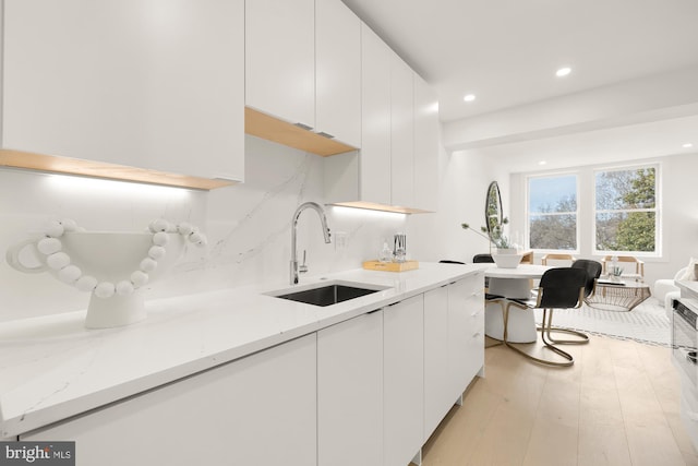 kitchen featuring light stone countertops, white cabinets, decorative backsplash, sink, and light hardwood / wood-style floors