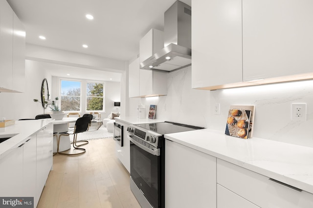 kitchen with white cabinetry, light hardwood / wood-style flooring, light stone countertops, stainless steel electric stove, and wall chimney exhaust hood