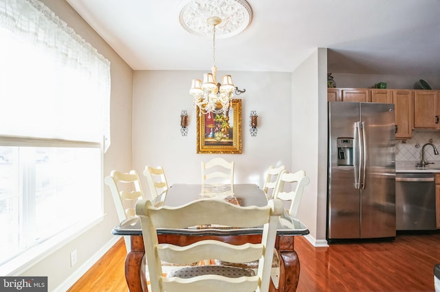 dining area featuring an inviting chandelier, wood finished floors, a healthy amount of sunlight, and baseboards