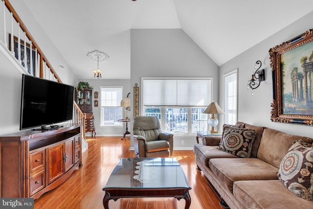 living room with a notable chandelier, light wood-style floors, baseboards, and high vaulted ceiling