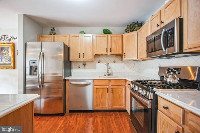 kitchen with wood finished floors, a sink, light countertops, appliances with stainless steel finishes, and tasteful backsplash