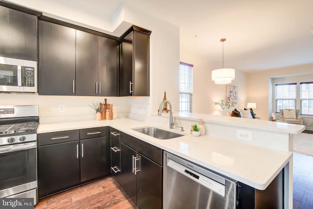 kitchen featuring decorative light fixtures, stainless steel appliances, light hardwood / wood-style floors, sink, and kitchen peninsula