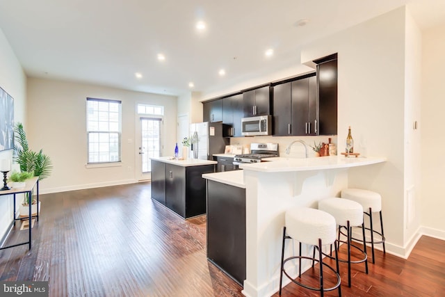 kitchen featuring a center island, stainless steel appliances, a kitchen breakfast bar, dark hardwood / wood-style floors, and kitchen peninsula