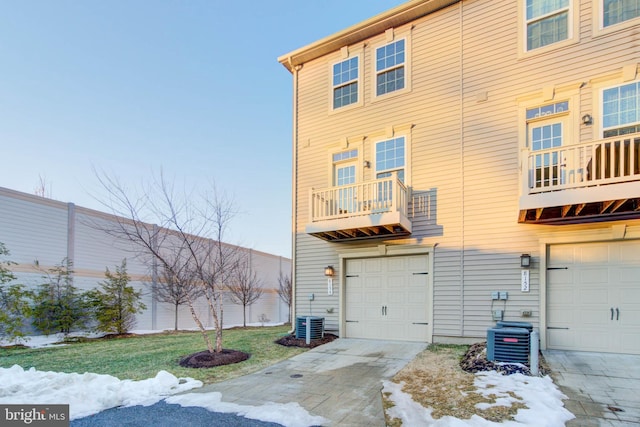 snow covered rear of property with a balcony, cooling unit, and a garage