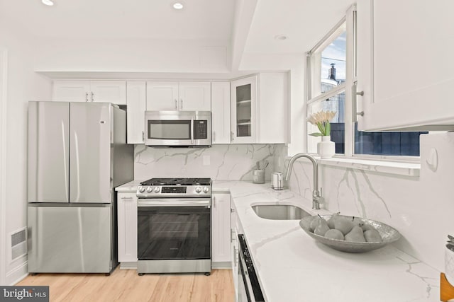 kitchen with stainless steel appliances, white cabinetry, light stone counters, and sink