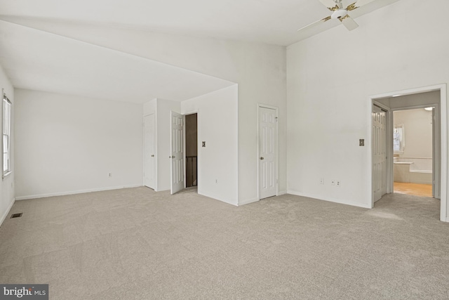 unfurnished bedroom featuring light carpet, multiple windows, ensuite bathroom, and ceiling fan