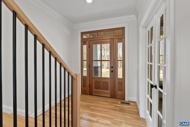 foyer entrance with light hardwood / wood-style flooring, crown molding, and french doors