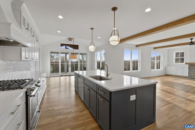 kitchen featuring white cabinetry, custom exhaust hood, an island with sink, hanging light fixtures, and sink