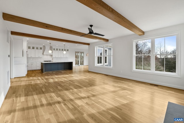 unfurnished living room with ceiling fan and beamed ceiling