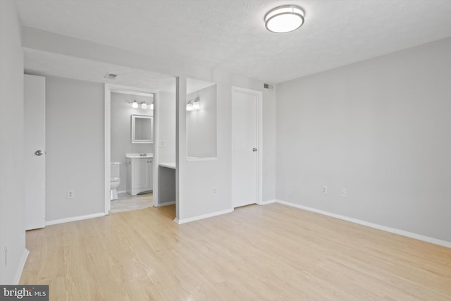 unfurnished bedroom with ensuite bath, a textured ceiling, and light wood-type flooring