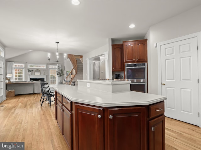 kitchen featuring light countertops, hanging light fixtures, double oven, a kitchen island, and light wood-type flooring