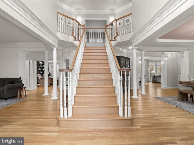 stairway featuring ornamental molding, a high ceiling, wood finished floors, and decorative columns