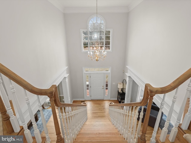 entrance foyer featuring light wood-type flooring, stairs, ornamental molding, and a notable chandelier