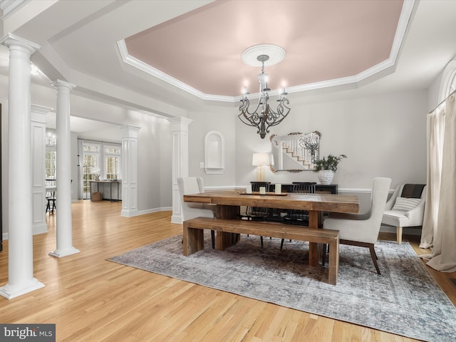 dining space with light wood-style floors, a raised ceiling, and ornate columns