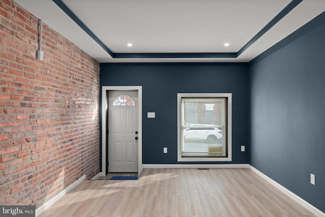 foyer with brick wall, light hardwood / wood-style flooring, and a raised ceiling