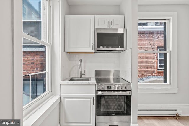 kitchen featuring a baseboard radiator, white cabinets, stainless steel appliances, sink, and light wood-type flooring