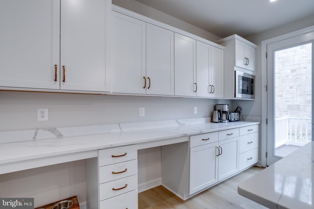 kitchen featuring built in desk, built in microwave, white cabinets, light stone counters, and light wood-type flooring