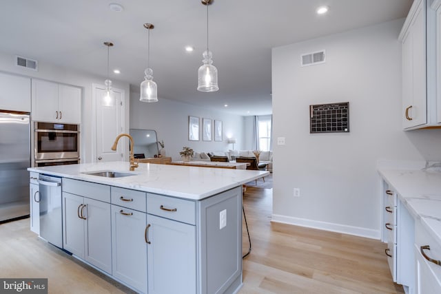 kitchen with sink, white cabinetry, hanging light fixtures, an island with sink, and stainless steel appliances