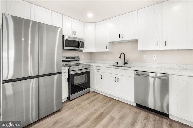 kitchen featuring light stone countertops, appliances with stainless steel finishes, white cabinetry, sink, and light wood-type flooring