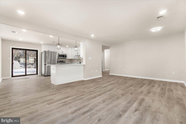 kitchen featuring appliances with stainless steel finishes, white cabinetry, light hardwood / wood-style floors, hanging light fixtures, and kitchen peninsula