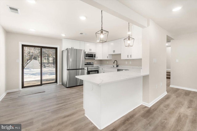 kitchen with white cabinets, stainless steel appliances, sink, hanging light fixtures, and light wood-type flooring