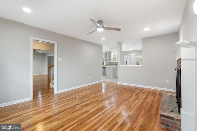 unfurnished living room with a brick fireplace, ceiling fan, and light wood-type flooring