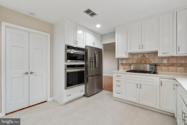 kitchen with decorative backsplash, white cabinets, and appliances with stainless steel finishes